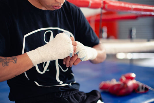 Boxer wrapping his hands with cotton hand wraps beside a boxing ring