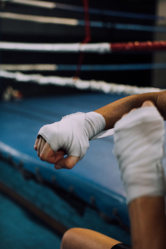 Boxer's hand wrapped in white cotton wraps beside a boxing ring