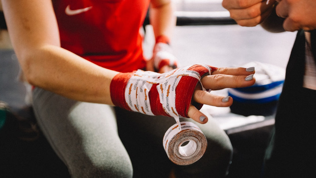 Woman in red shirt wrapping her hand with red and white boxing hand wraps in a gym