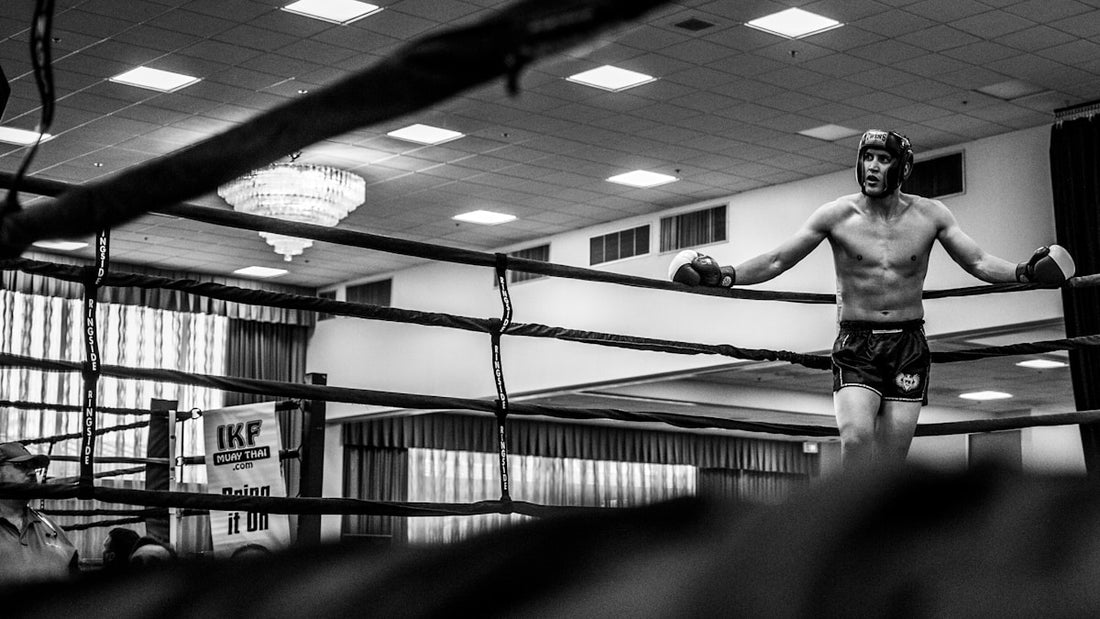 Black and white photo of a boxer in headgear leaning on the ring ropes