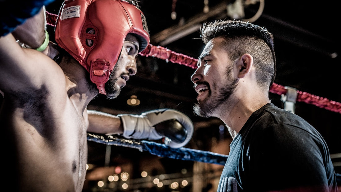 Boxing coach in dark gym giving instructions to a fighter wearing red headgear