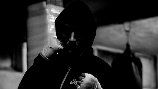 Boxer in hoodie with hand wraps visible in a dark gym atmosphere